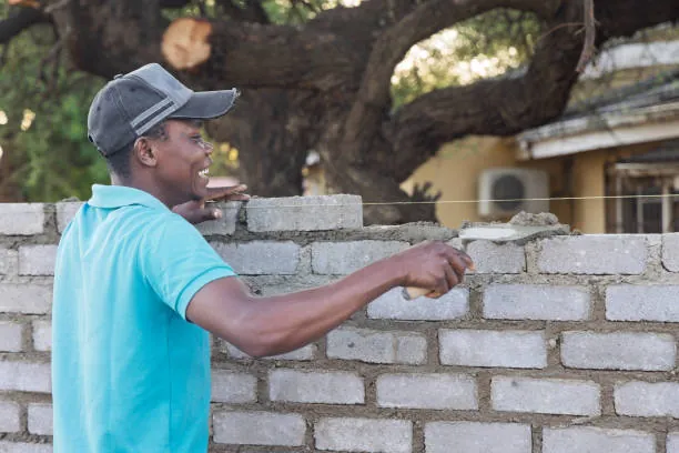 a-builder-in-a-blue-shirt-applying-mortar-to-a-partially-built-brick-wall-for-owaid-orphan-and-widow-support